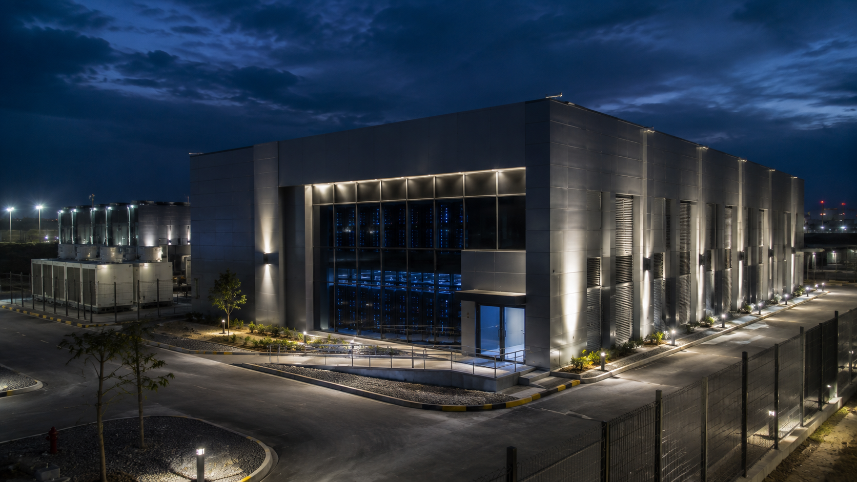 A data centre at blue hour, server halls glowing behind a glazed facade.